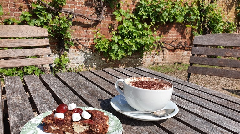 coffee and rocky road cake on outdoor table with a traditional brick wall with vines behind